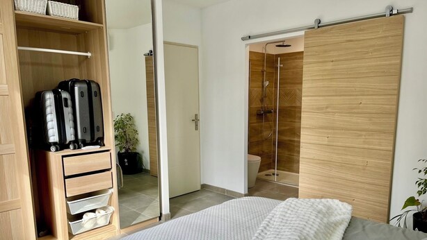 Une chambre avec un lit, une armoire, une salle de bain avec douche et un placard où ranger les bagages.