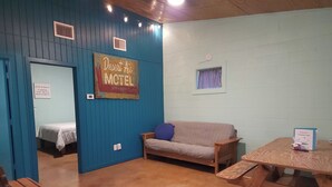 A motel room with a blue wall, a wooden sofa, a small table, and a bed with a white comforter.