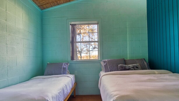 A small, cozy room with two single beds, a window with curtains, and teal walls.