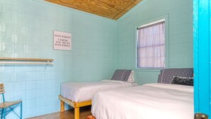 A room with two beds, a wooden ceiling fan, a window with checkered curtains, and a sign on the wall.