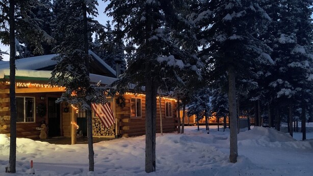 A log cabin with a snow-covered roof, surrounded by trees and a snow-covered ground. - Burnt Paw House-Modern Comfort in the Last Frontier (For families or casual travelers) (Tok)