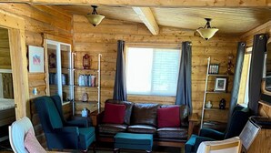 A cozy log cabin interior with a wooden floor, a sofa set, two armchairs, a coffee table, and a bookshelf. - Burnt Paw House-Modern Comfort in the Last Frontier (For families or casual travelers) (Tok)