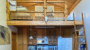 A loft-style kitchen with wooden cabinets, a central island, and a dining area with a table and chairs. - Burnt Paw House-Modern Comfort in the Last Frontier (For families or casual travelers) (Tok)