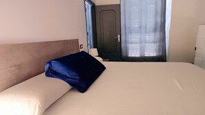 A hotel room with a bed, a nightstand, a door, and a window with blinds. - Al Porto Antico (Genoa)