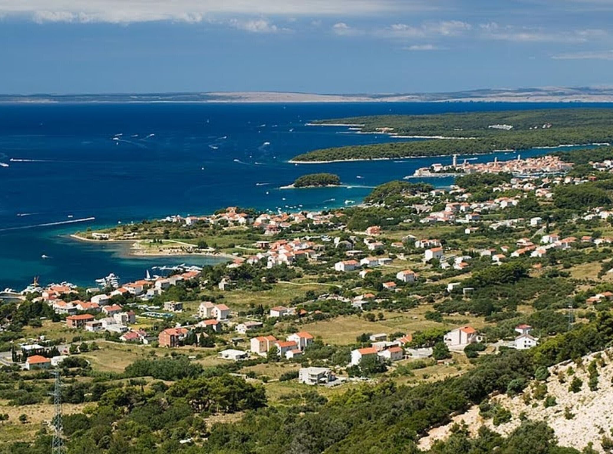 Una località costiera con case e edifici lungo la riva, un faro e barche nell'acqua.