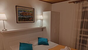 Un dormitorio ordenado con cama, almohadas, una lámpara de noche, un armario y un cuadro en la pared.