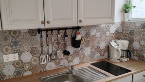 A kitchen with white cabinets, a patterned backsplash, a stainless steel sink, a coffee maker, and hanging utensils. - Villa Mery - Studio Apartment with Balcony and Sea View - 3 (Rab)