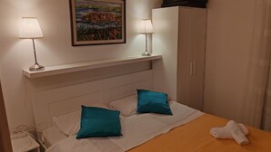 A neatly made bed with two pillows, a bedside table with a lamp, a painting on the wall, and a wardrobe. - Villa Mery - Studio Apartment with Balcony and Sea View - 3 (Rab)