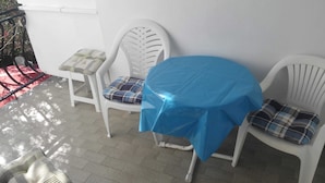 A small outdoor seating area with two white plastic chairs and a round table covered with a blue tablecloth.