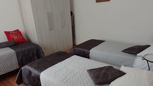 Ein Zimmer mit zwei Betten, jeweils mit grau-weißer Bettdecke und einem roten Zierkissen.