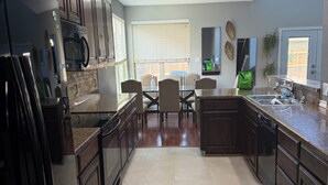 Una cocina con armarios de madera oscura, encimera de granito, una mesa de comedor con sillas y una ventana con persianas.