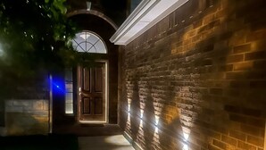 Un sendero que lleva a una puerta, con un muro de ladrillo a un lado y un árbol al otro.
