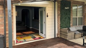 Un garaje con una puerta entreabierta, una alfombra colorida y un banco de mimbre en el exterior.