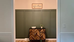 A reception area with a 'WELCOME' sign, a wooden herringbone cabinet, and a small plant on a black console table.