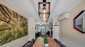 A dining room with a wooden table, chairs, a large painting, and a ceiling light fixture. - Lakefront-Fish&Kayak-FirePit-hottub-walk to bars (Lake Harmony)