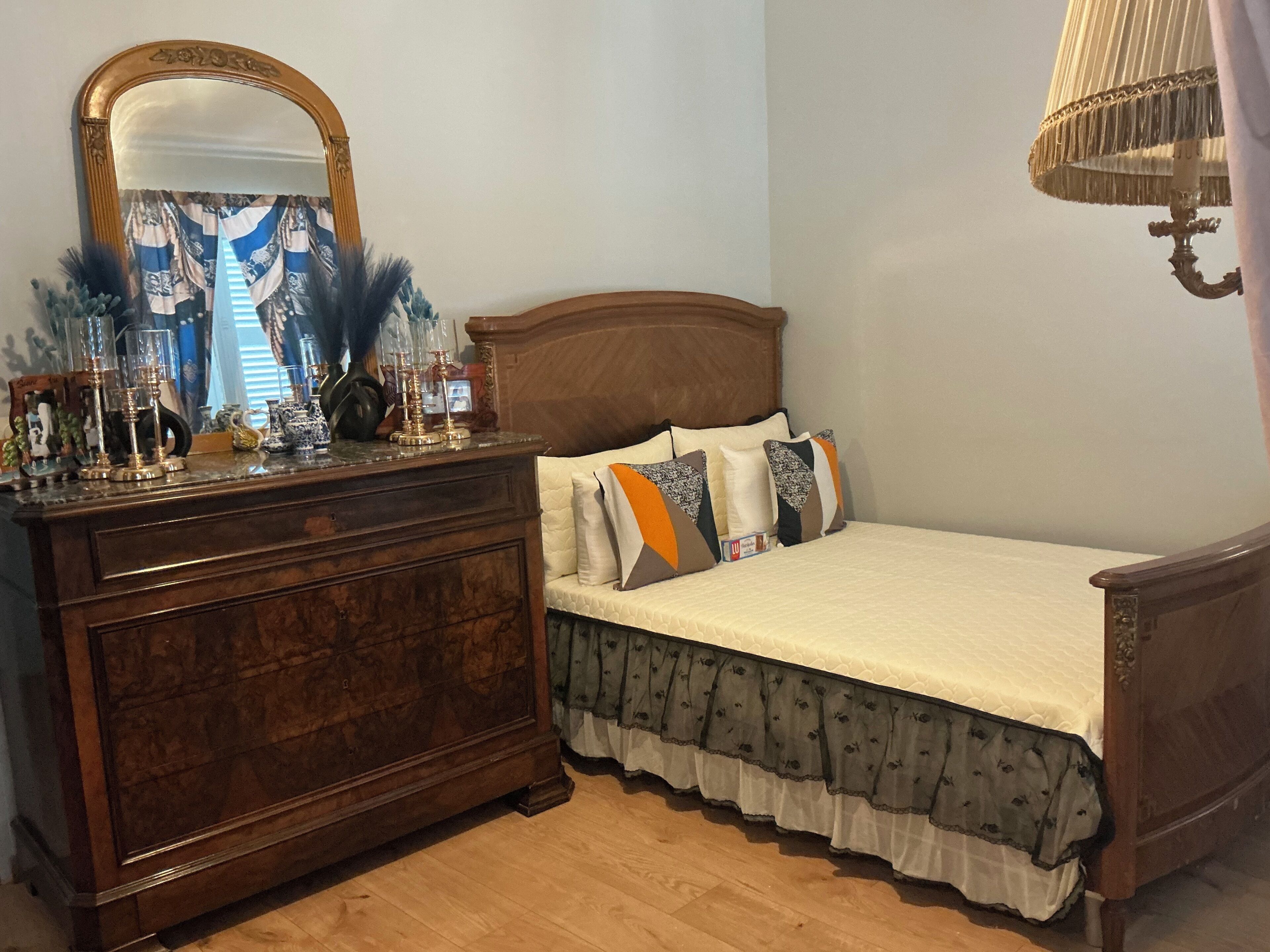 Ein Schlafzimmer mit einem hölzernen Schminktisch, einem Bett mit gemusterten Kissen, einem Spiegel und einer Lampe.