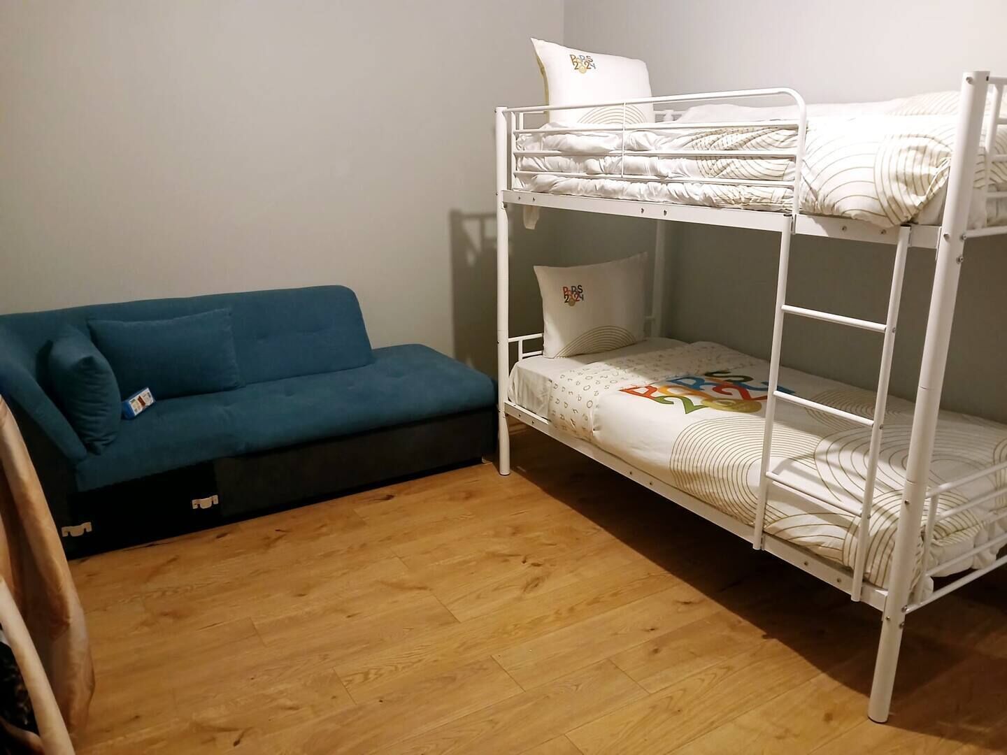 Ein Etagenbett mit weißer Matratze und Kissen, ein blaues Sofa mit Sitzkissen und ein Holzboden.