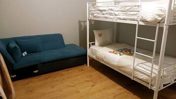 Ein Etagenbett mit weißer Matratze und Kissen, ein blaues Sofa mit Sitzkissen und ein Holzboden.