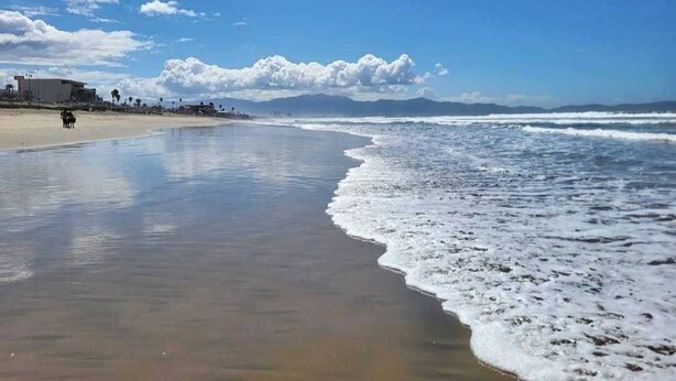 Une plage avec un ciel dégagé, des vagues et quelques personnes qui se promènent.