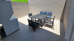 Une terrasse avec une table et des chaises, un meuble blanc et un mur vert.