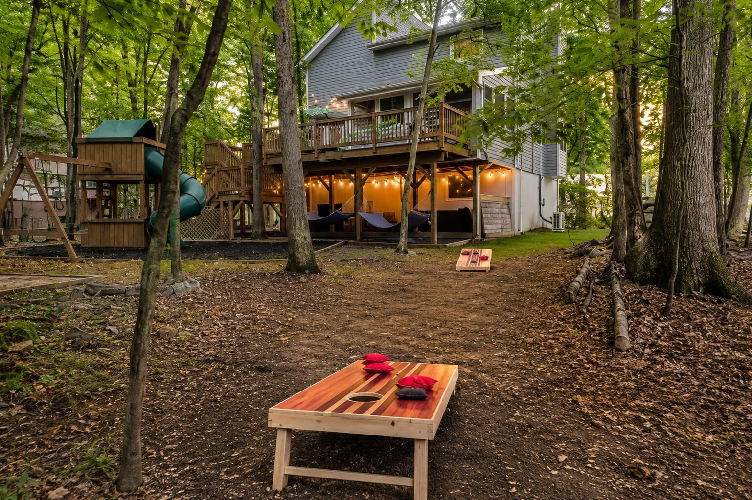 Een huis met een terras, een schommel en een picknicktafel in een bebost gebied.