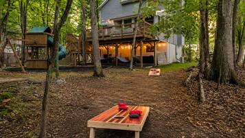 Een huis met een terras, een schommel en een picknicktafel in een bebost gebied.