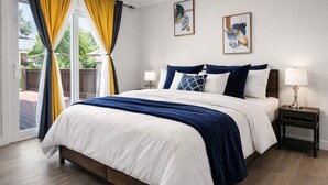 A bedroom with a bed, two bedside tables with lamps, a window with yellow curtains, and two wall art pieces.
