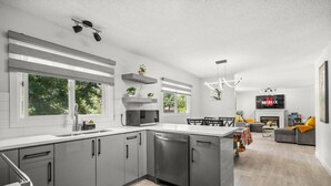 A modern kitchen with grey cabinets, a central island, and a dining area with a sofa and TV.