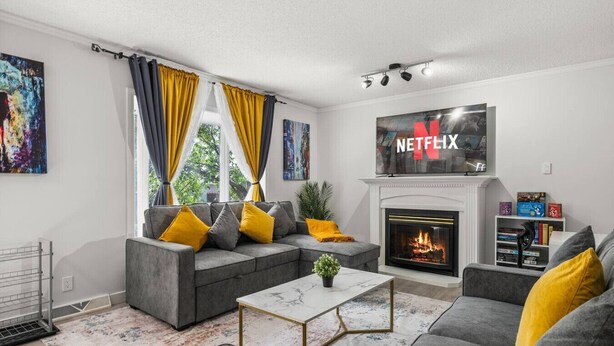 A modern living room with a gray sofa, yellow cushions, a fireplace, and a large TV screen displaying "NETFLIX".