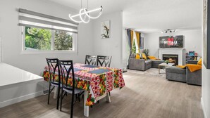 A modern living room with a fireplace, a dining area with a colorful tablecloth, and a TV mounted on the wall.
