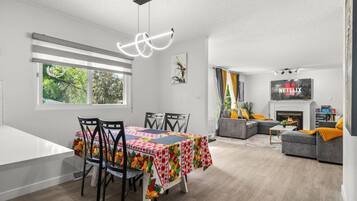 Una sala de estar moderna con chimenea, un comedor con mantel colorido y un televisor montado en la pared.