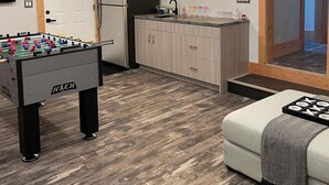 A cozy room with a foosball table, a kitchenette with a refrigerator, and a sofa.