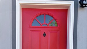 A red door with a small window above it, a black doorbell, and a black mail slot.