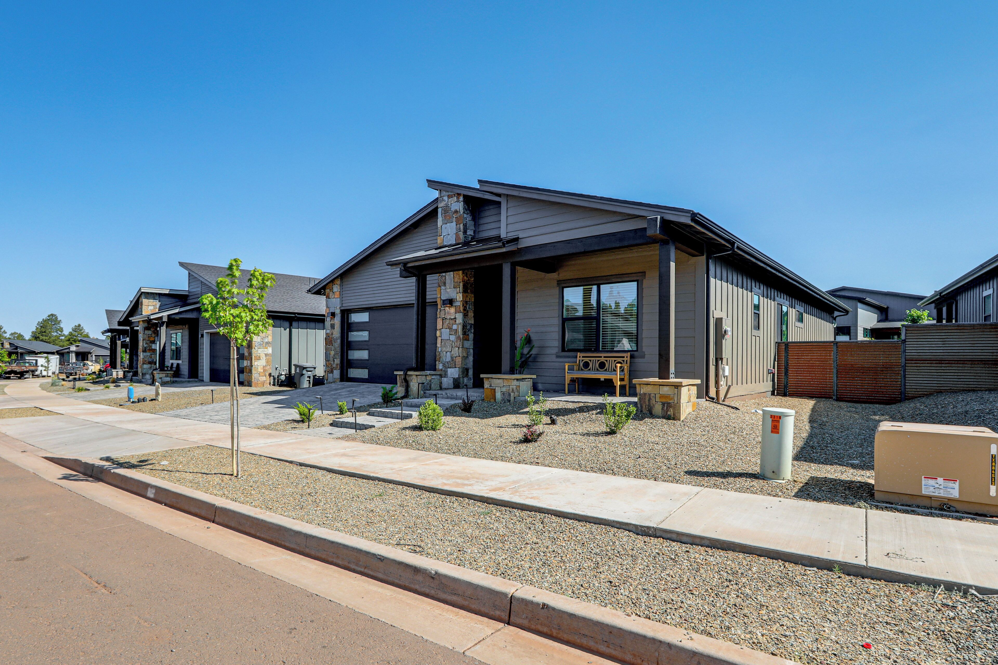 A modern two-story house with a stone facade, a covered porch, and a small garden area.