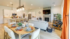 Een moderne keuken met witte kasten, een eethoek met een houten tafel gedekt voor vier personen, en een woonkamer met een bank en een open haard.