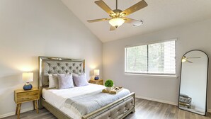 Un dormitorio con cama, mesitas de noche, ventilador de techo, ventana con persianas y espejo.