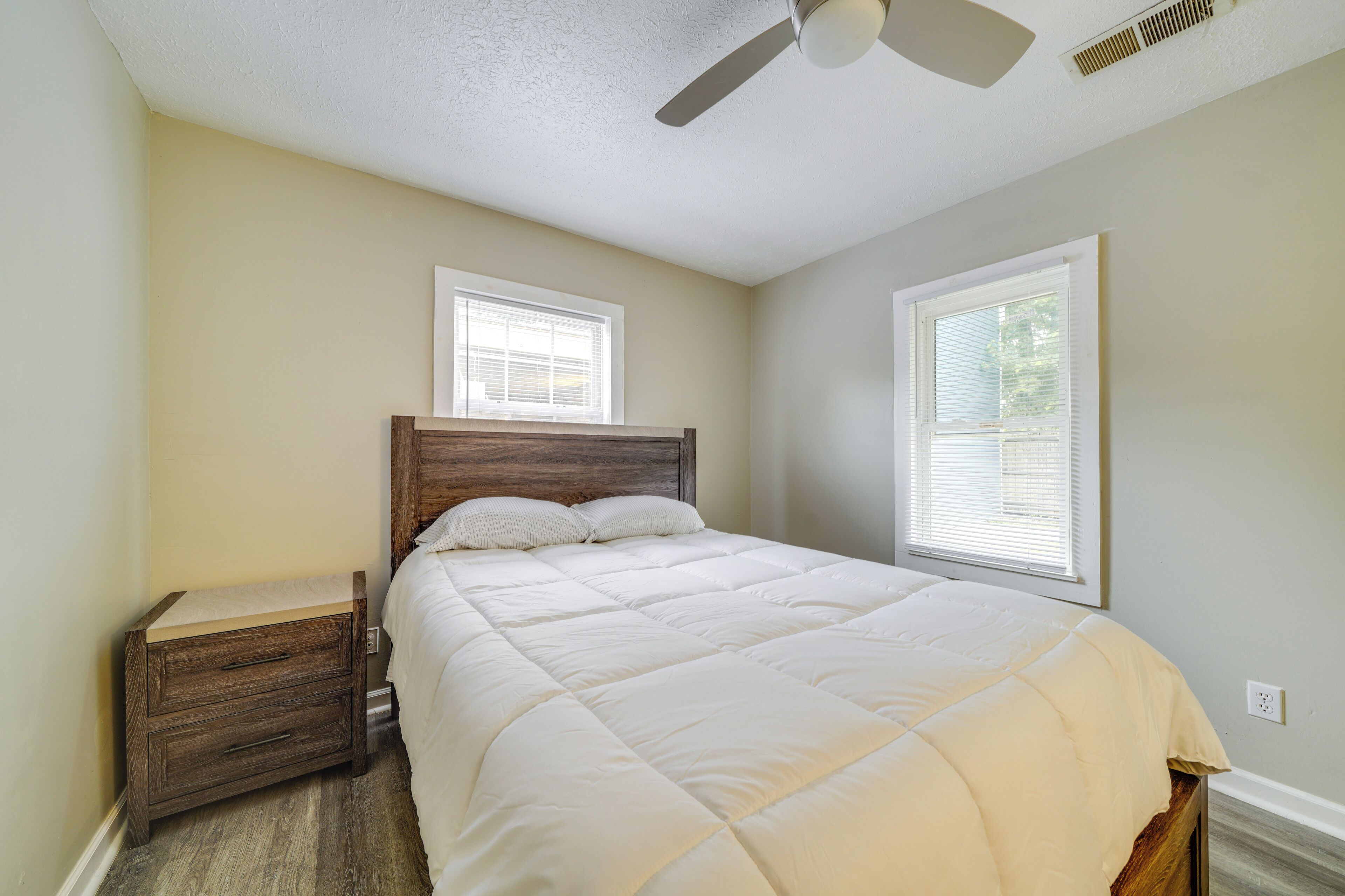 A bedroom with a bed, nightstand, and two windows.