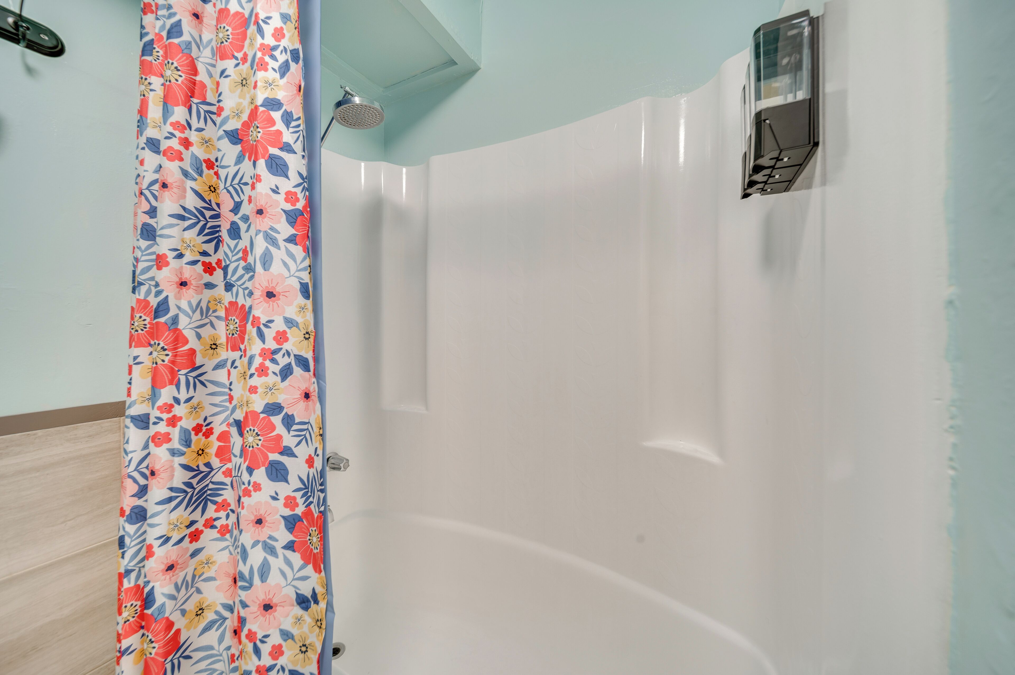 Douchegedeelte met een bloemen gordijn, een witte betegelde wand en een klein raam met bedieningspaneel.
