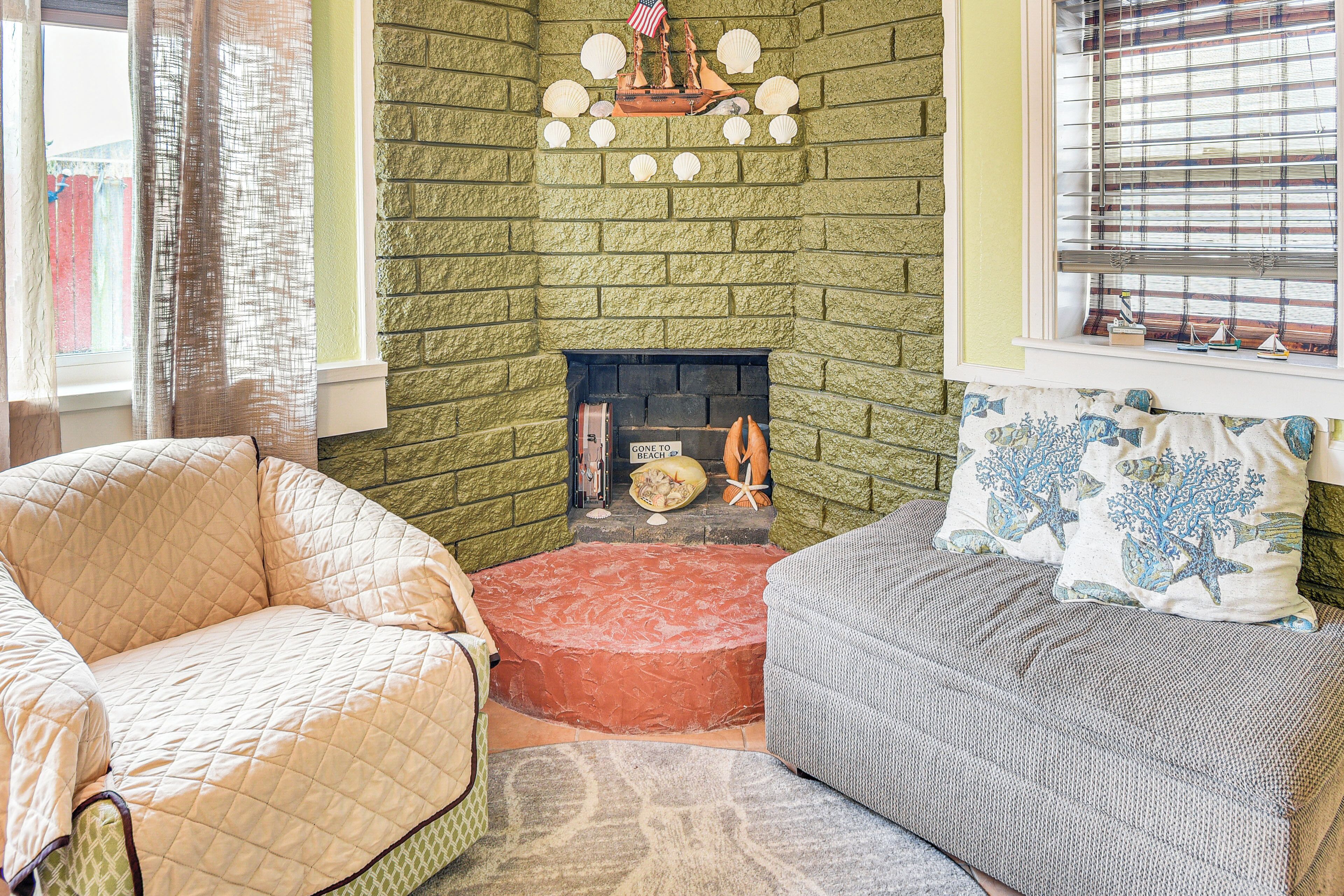 A cozy living room with a green brick fireplace, a comfortable beige armchair, and a gray sofa with decorative pillows.