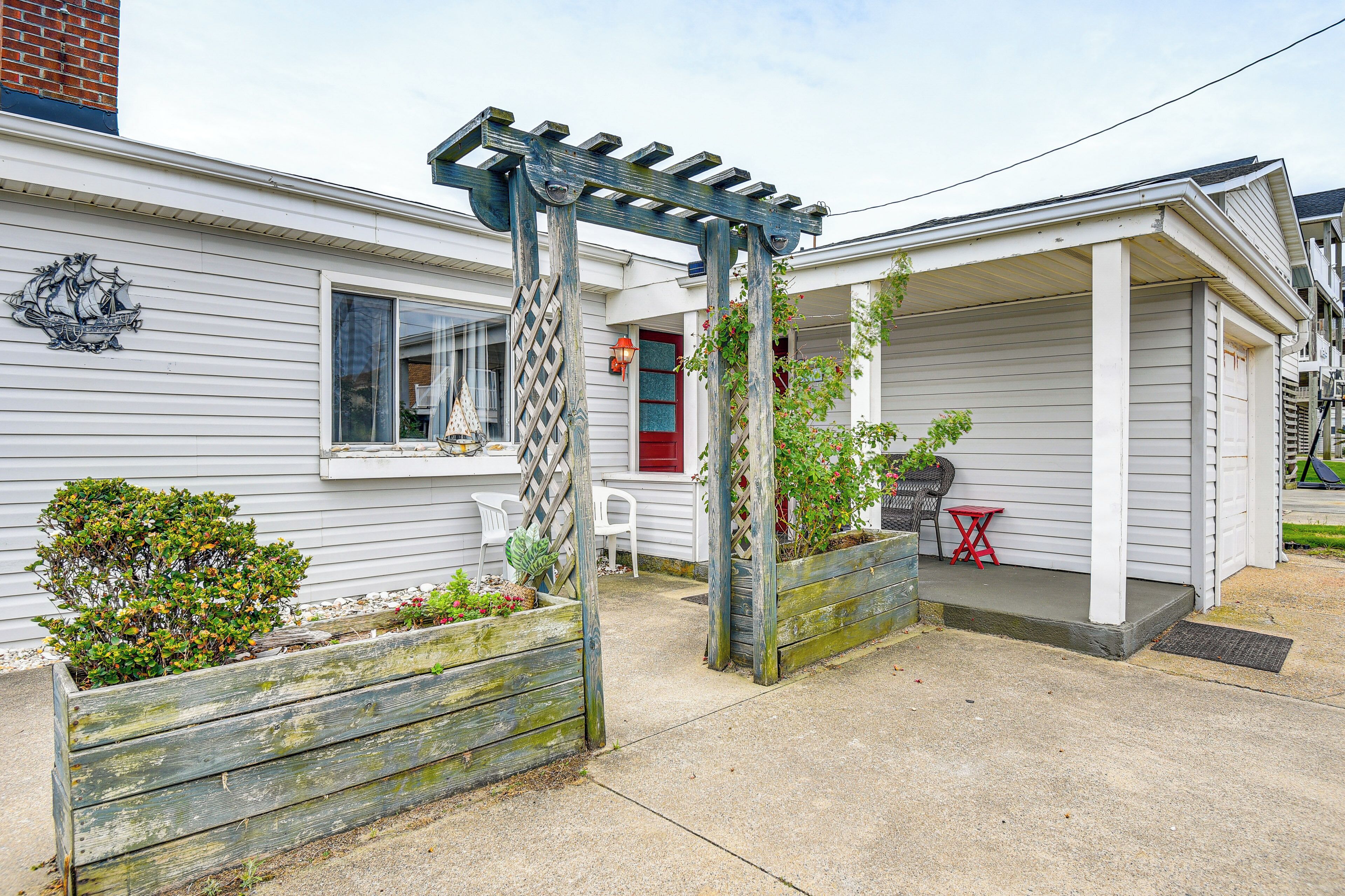 A residential property with a covered porch, a wooden pergola, and a small garden area with plants and a bench.