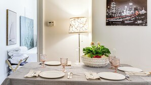 Ein Essbereich mit kariertem Tischläufer, einem ordentlich gedeckten Tisch mit Tellern, Gläsern und Besteck, einer floralen Tischdekoration und einem Stadtbildgemälde an der Wand.