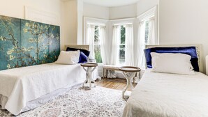 Ein Schlafzimmer mit zwei Betten, einem großen floralen Wandbild und Blick auf Grün durch die Fenster.