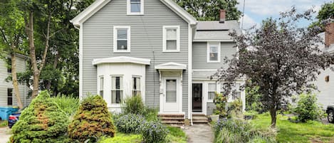 Une maison à deux étages avec un porche à l’avant, un garage et un jardin bien entretenu.