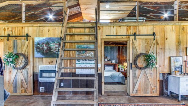 Un interno rustico con pareti in legno, una zona mansardata, un letto e una scala che conduce a una mansarda.