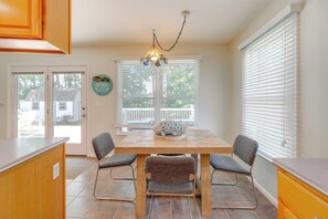Une cuisine avec une table et des chaises en bois, un luminaire suspendu et une fenêtre avec des stores.