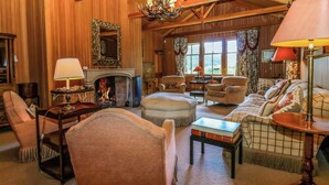 A cozy, wood-paneled living room with a fireplace, comfortable seating, and a chandelier. - Creag Bhalg (Ballater)