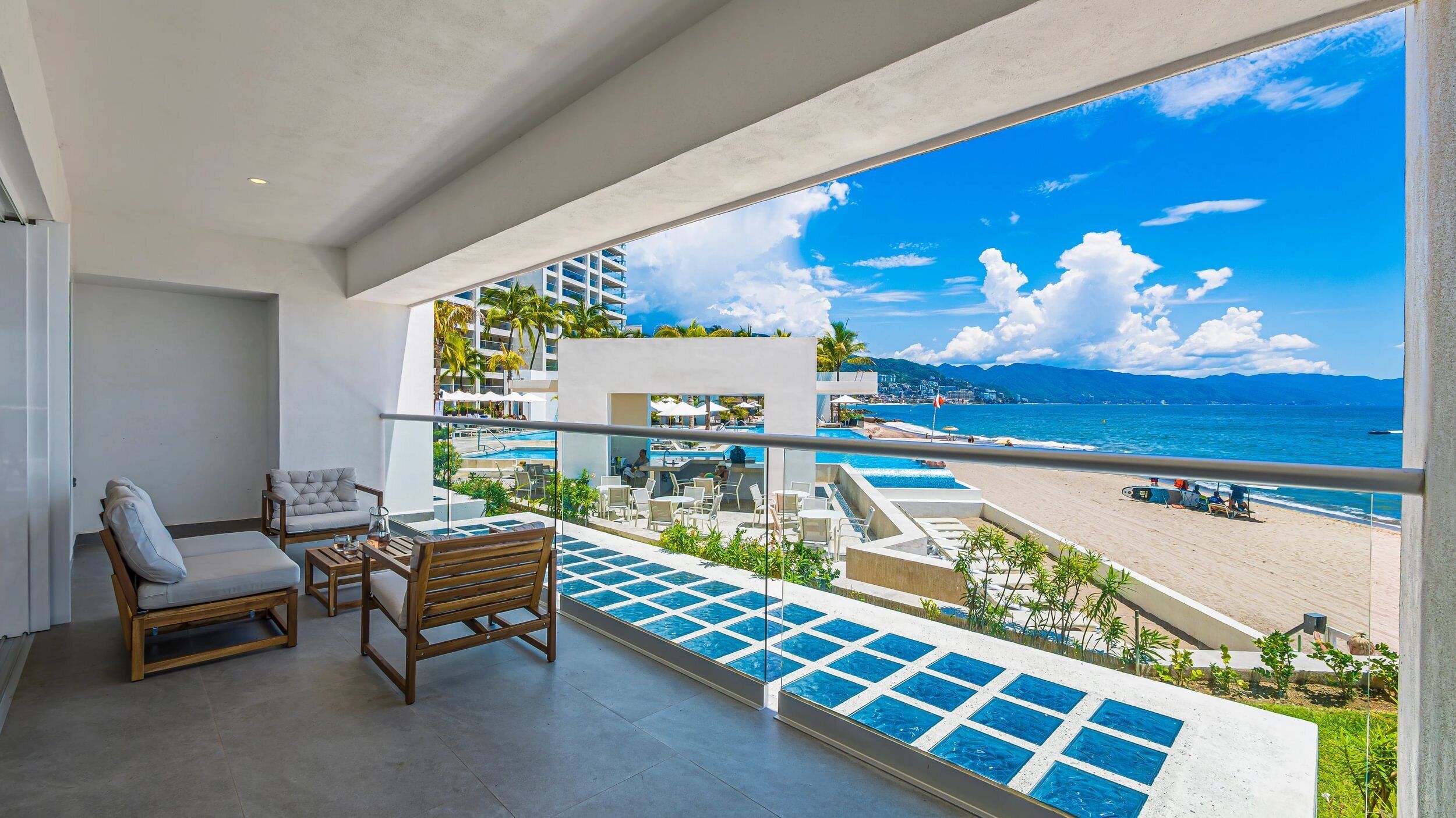 Un balcon avec vue sur la plage et l’espace piscine, comprenant des chaises longues et une petite table.