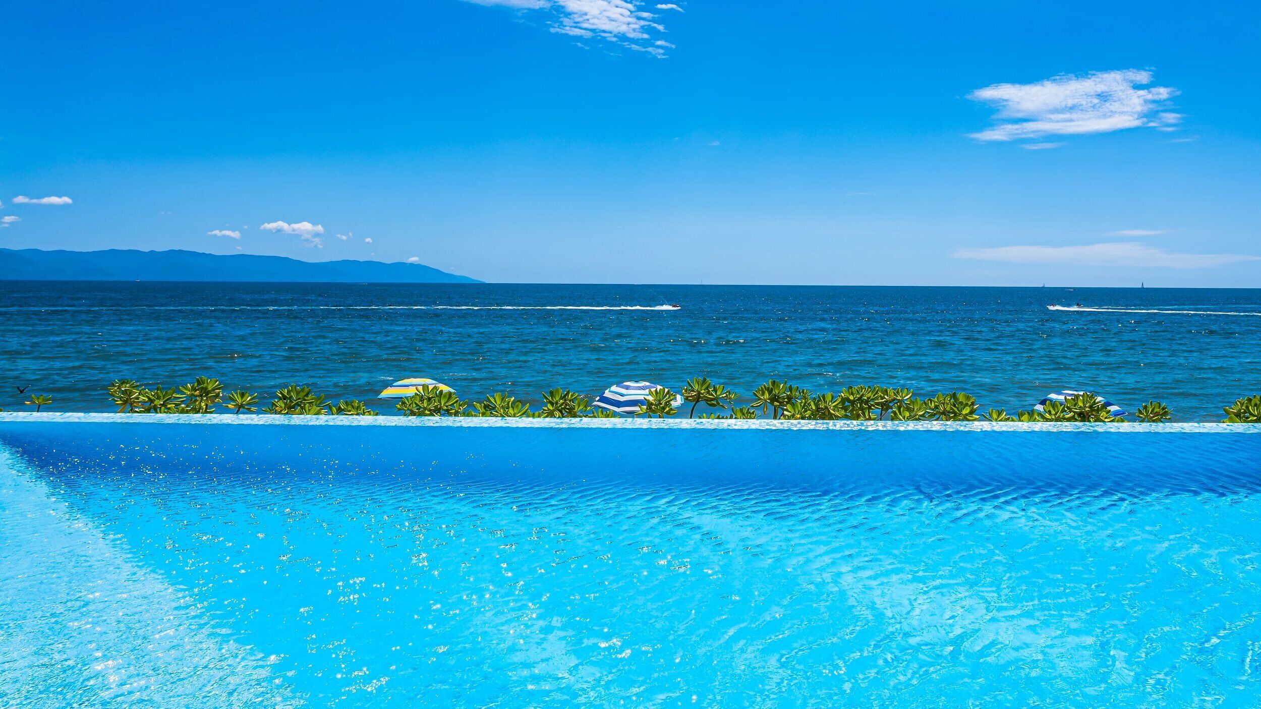 Una piscina azul cristalina con vista al océano y montañas distantes.