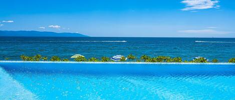 Una piscina azul cristalina con vista al océano y montañas distantes.