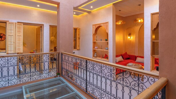 Een hotelkamer met een glazen vloer, een balkon met sierhekwerk en een rode bank in de zithoek.